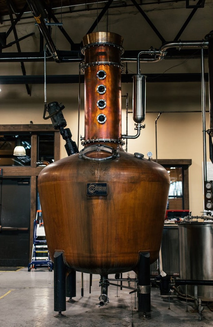 A copper distillation apparatus in an indoor industrial setting, showcasing brewery equipment.